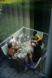 Eine Gruppe von Freunden, die um einen Tisch versammelt sind, von oben durch ein Fenster gesehen, genießen eine gemeinsame Mahlzeit - MASF40878