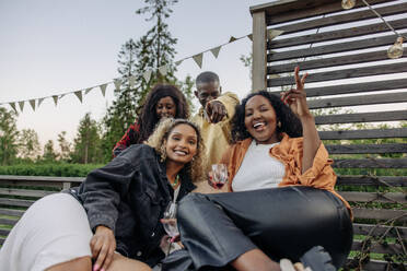 Portrait of woman showing peace sign while enjoying with male and female friends during party in back yard - MASF40912