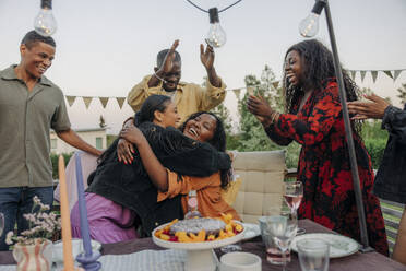 Zwei Frauen umarmen sich herzlich, während sie im Hinterhof, umgeben von Freunden und Familie, einen Geburtstag feiern - MASF40917