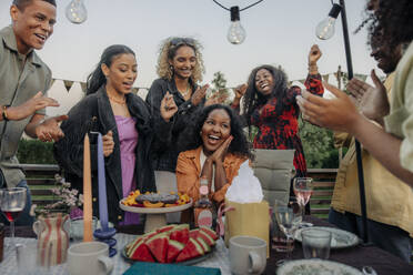 A group of happy friends celebrate a birthday outdoors, surrounded by both male and female companions, cheering and clapping - MASF40924