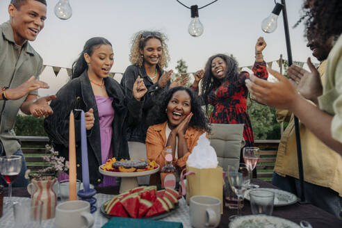 Eine Gruppe von glücklichen Freunden feiert einen Geburtstag im Freien, umgeben von männlichen und weiblichen Begleitern, die jubeln und klatschen - MASF40924