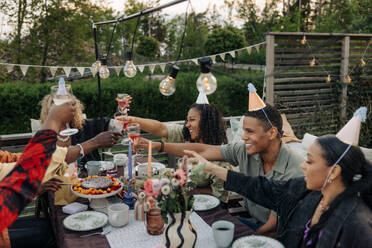 Eine Gruppe von fröhlichen Freunden feiert einen Geburtstag im Freien, genießt Getränke und strahlt vor Glück - MASF40937