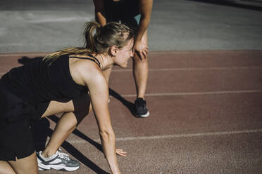 A young woman prepares to sprint on a running track, captured in a dynamic side angle shot - MASF40977