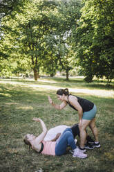 Eine Trainerin freut sich mit einer Frau auf der Wiese nach einer produktiven Trainingseinheit im Park - MASF40981