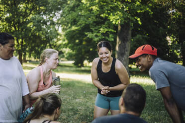 Eine Gruppe von Freunden, darunter eine fröhliche Frau, trifft sich nach dem Training inmitten des üppigen Grüns des Parks - MASF40984