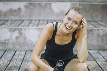 Eine Frau sitzt glücklich auf einer Treppe und lacht mit einem ansteckenden Lächeln - MASF40999