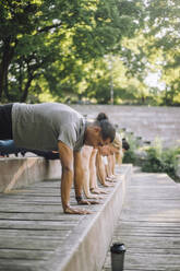 Friends motivate each other during a city workout, performing push-ups on steps with a stunning urban view - MASF41003