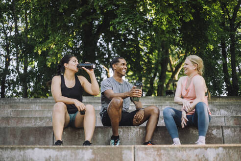 Freunde, die nach dem Training eine Pause machen, Wasser trinken und sich unterhalten, während sie in einem niedrigen Blickwinkel sitzen. - MASF41012