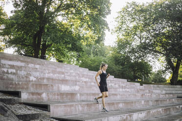 Eine ruhige Parklandschaft bildet die Kulisse für eine junge Frau, die anmutig eine Treppe hinabsteigt - MASF41023