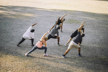 Team doing stretching with female instructor at park - MASF41029