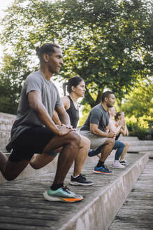 Männliche und weibliche Freunde unterstützen sich gegenseitig bei ihren Fitnesszielen mit präzisen Ausfallschritten auf einer Treppe - MASF41030