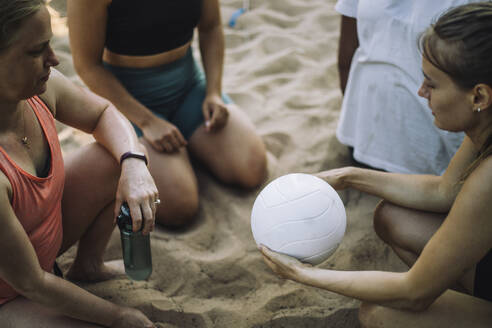 Eine Frau bereitet sich darauf vor, einen Volleyball aufzuschlagen, während ihre Freunde auf dem Sandplatz warten (Vogelperspektive) - MASF41049