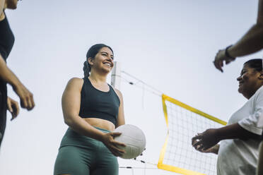 Eine Gruppe von Freunden genießt ein Volleyballspiel an einem sonnigen Tag, mit einer glücklichen Frau in Aktion - MASF41057