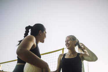 Eine Gruppe glücklicher Frauen genießt das gemeinsame Volleyballspiel bei Sonnenschein und blauem Himmel - MASF41058