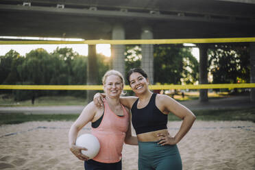 Zwei fröhliche Frauen umarmen sich, während sie einen Volleyball halten, und strahlen dabei Glück und Positivität aus - MASF41065