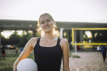 Eine strahlende junge Frau zeigt selbstbewusst einen Volleyball, während sie einen freudigen Ausdruck trägt - MASF41070