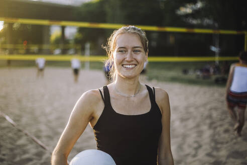 Eine glücklich strahlende Frau hält einen Volleyball und blickt mit einem strahlenden Lächeln in die Ferne - MASF41071