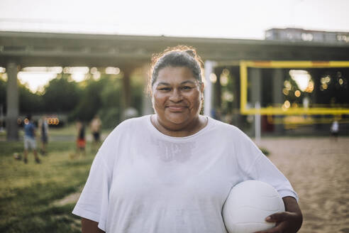 Selbstbewusste Plus-Size-Frau strahlt Freude aus, während sie mit einem Volleyball posiert und ihr schönes Lächeln zur Schau stellt. - MASF41073