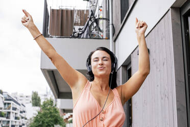 Eine Frau tanzt voller Freude mit erhobenen Armen zum Rhythmus der Musik auf ihrem Balkon - MASF41076