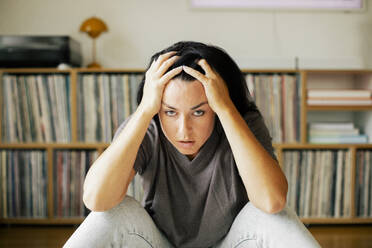 Eine Frau, die unter Stress und Ängsten leidet, nimmt sich einen Moment Zeit, um sich zu sammeln, indem sie ihren Kopf zu Hause in die Hände stützt - MASF41083