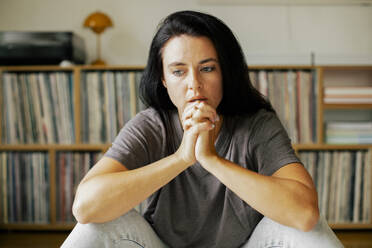 A woman sits at home, her hands clasped together in anxiety and concern, reflecting the stress of modern life - MASF41084