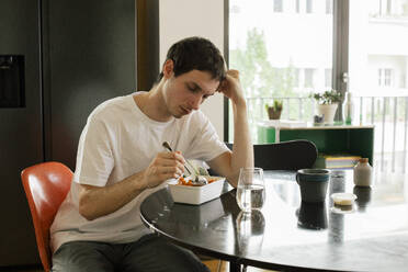 Ein Mann sitzt entmutigt am heimischen Tisch und stützt sich beim Essen auf seinen Ellbogen - MASF41090