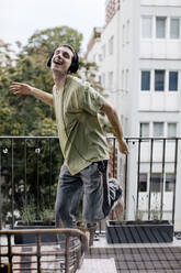 Carefree man listening to music while dancing in balcony - MASF41092