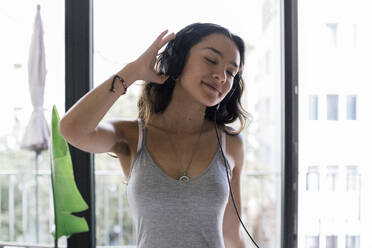 Carefree young woman listening to music through headphones at home - MASF41113