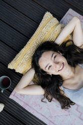 Eine Frau genießt einen ruhigen Moment auf ihrem Balkon, lächelt und ruht sich mit den Händen hinter ihrem Kopf aus - MASF41117
