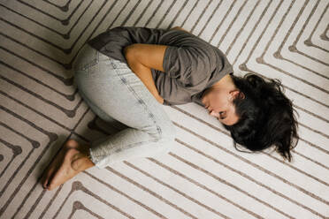 A lone individual seeks comfort in a fetal position on a soft home rug - MASF41133