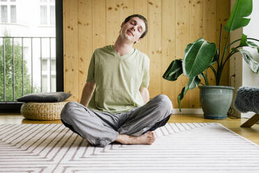 Ein Mann übt Yoga-Dehnübungen auf einem bequemen Teppich zu Hause, um einen gesunden und ruhigen Lebensstil zu fördern. - MASF41146