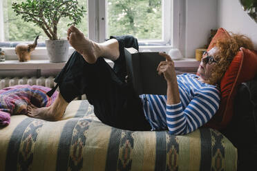 Eine heitere Seitenansicht einer älteren Frau, die sich zu Hause auf ihrem Bett mit einer guten Lektüre entspannt - MASF41169