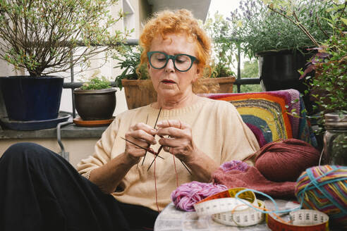 Eine ältere Frau frönt ihrer Leidenschaft für das Stricken und fertigt auf ihrem Balkon einen warmen und bequemen Pullover - MASF41174
