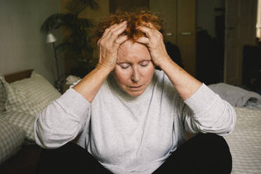 Emotional verzweifelte ältere Frau sucht Trost, indem sie ihren Kopf in ihren Händen stützt, während sie in ihrem Schlafzimmer sitzt - MASF41180