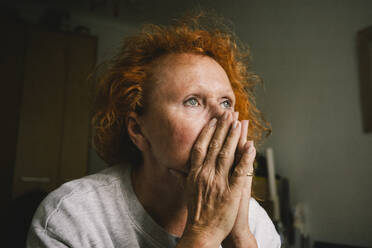 In Gedanken versunkene ältere Frau, die in der Einsamkeit ihres Hauses sitzt und sich das Gesicht hält - MASF41183