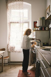 An elderly lady pouring milk into a container in her kitchen, as seen from a side angle - MASF41189