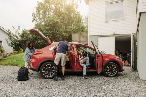 Eine Familie packt ihr umweltfreundliches Elektroauto mit ihren Habseligkeiten vor ihrem Haus, bereit für eine nachhaltige Reise - MASF41201