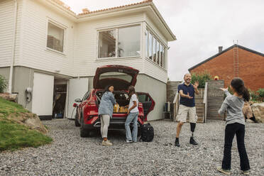 Eine glückliche Familie, die sich neben ihrem vor dem Haus geparkten Elektrofahrzeug amüsiert - MASF41204
