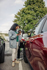 Eine Mutter und ihre Tochter lächeln, während sie ihr Elektroauto aufladen und so ihren Beitrag zu einem grüneren Planeten leisten - MASF41214