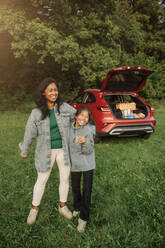 A mother and daughter bond over a playful moment by their car in the park, radiating pure joy and happiness - MASF41236