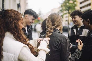 Teen girl skillfully braids friend's hair on a busy street, showcasing their strong bond and trust - MASF41256