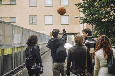 Eine Gruppe von Freunden spielt lässig Basketball, während sie den Bürgersteig entlang schlendern, wobei ein Jugendlicher die Führung übernimmt - MASF41272