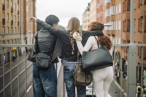 Männliche und weibliche Freunde genießen die Aussicht auf die Stadt, während sie gemeinsam an der Reling stehen - MASF41292