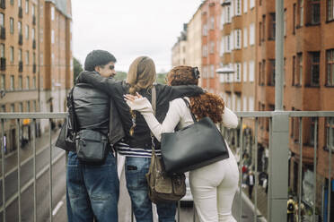 Drei Freunde genießen die Aussicht auf die Stadt, wobei ein Mädchen im Teenageralter ihre männlichen und weiblichen Begleiter von hinten umarmt - MASF41293