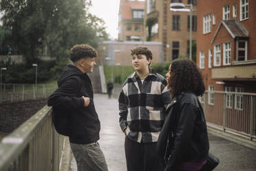 Teenage boy engaged in conversation with male and female friends on a sidewalk, captured from a side angle - MASF41295