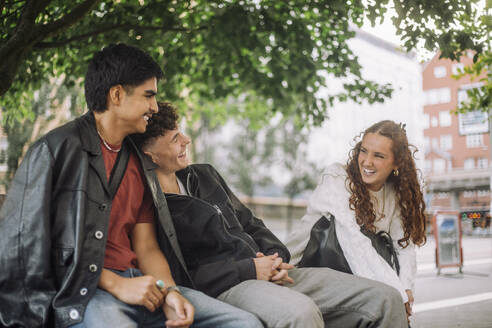 Eine Gruppe von Teenagern, die auf einer Parkbank sitzend die Gesellschaft der anderen genießen und gemeinsam lachen. - MASF41305