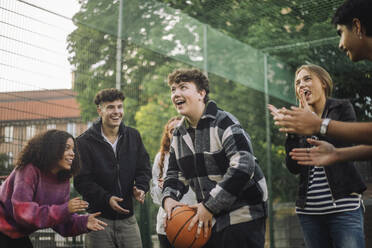 Eine Gruppe fröhlicher Freunde ermutigt einen Teenager, während er sich darauf vorbereitet, den Ball während eines Basketballspiels zu werfen - MASF41311