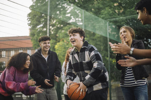 A group of joyful friends encourage a teenage boy as he gets ready to shoot the ball during a basketball game - MASF41311