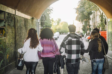 Male and female friends walking together through an underpass, seen from behind. - MASF41315