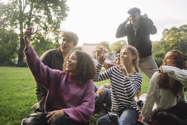 Fröhlicher Teenager hält Erinnerungen mit Freunden im Park fest und posiert für ein Gruppen-Selfie mit ihrem Smartphone - MASF41321